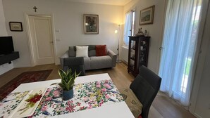 A living room with a sofa, a dining table with a floral tablecloth, a TV, and a plant. - Garden view in the heart of Prosecco Hills (San Vendemiano)
