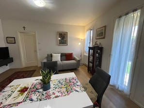 A living room with a sofa, a dining table with a floral tablecloth, a TV, and a plant. - Garden view in the heart of Prosecco Hills (San Vendemiano)