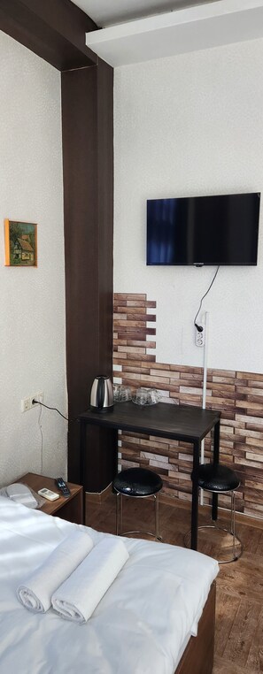 A hotel room with a bed, a desk with two chairs, a television mounted on the wall, and a wooden accent wall. - Sweet Hotel 1 (Tbilisi)