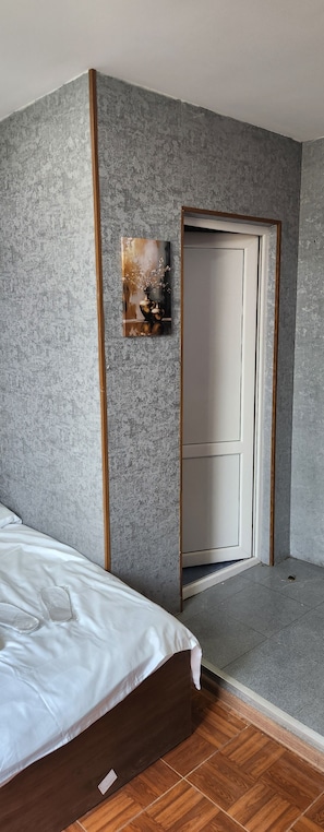 Un dormitorio con cama, una puerta y un pequeño cuadro en la pared.
