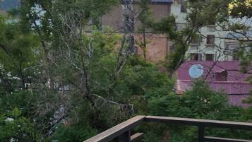 A balcony with a metal railing, concrete walls, and a view of buildings and trees in the background.