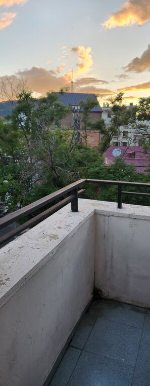 A balcony with a metal railing, concrete walls, and a view of buildings and trees in the background. - Sweet Hotel 1 (Tbilisi)