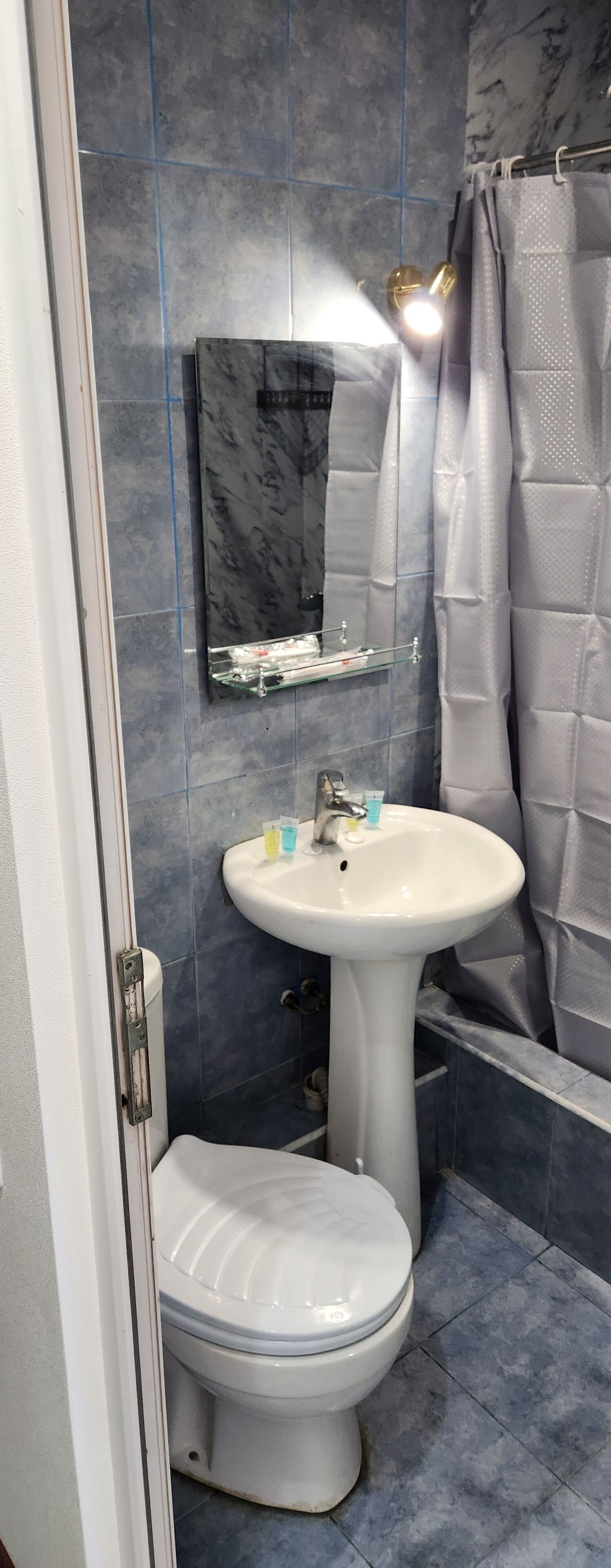 Une salle de bain avec un lavabo blanc, des toilettes, un miroir et un rideau de douche.