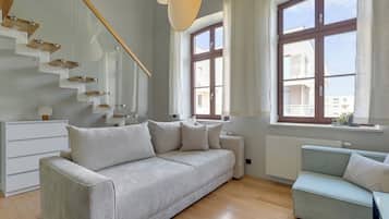 A modern living room with a sofa, a smaller armchair, a staircase, and large windows.