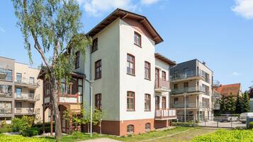 A multi-story residential building with a mix of balconies and windows, surrounded by greenery and other buildings.