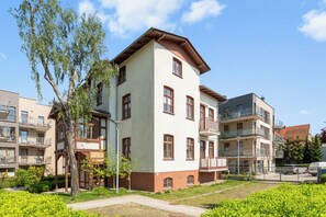Un edificio residencial de varios pisos con una combinación de balcones y ventanas, rodeado de vegetación y otros edificios.
