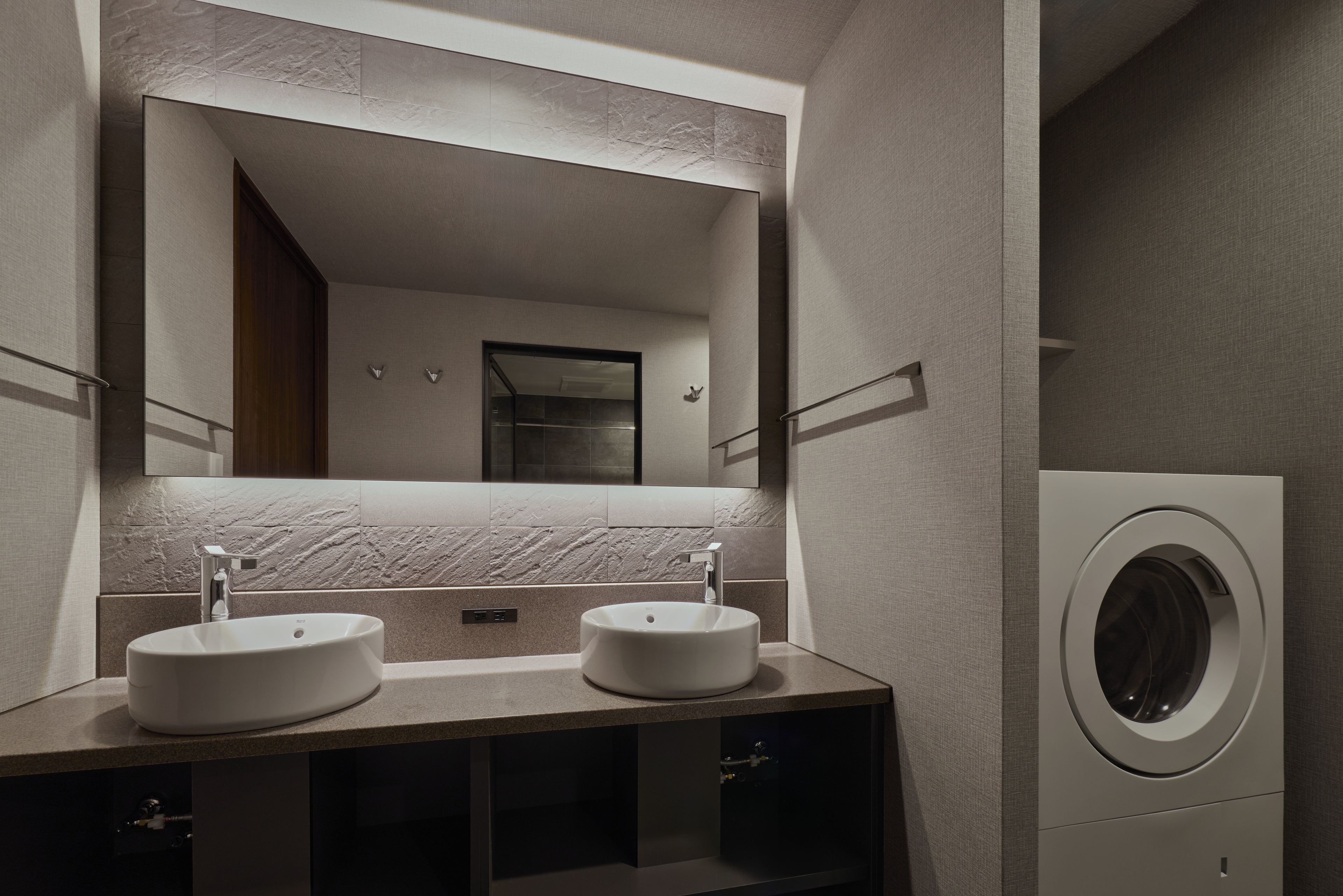 A modern bathroom with two sinks, a large mirror, and a built-in washing machine.