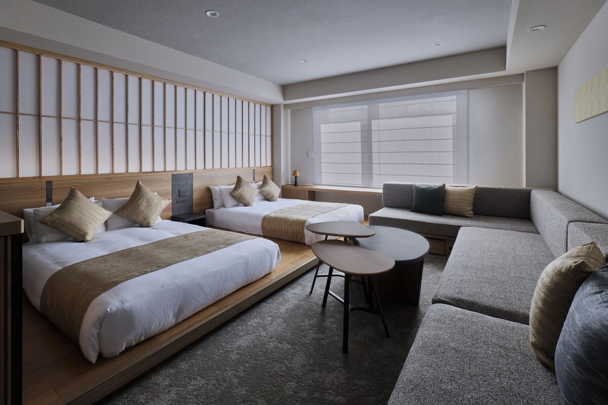 A hotel room with two beds, a sofa, a small table, and a view of the outside.