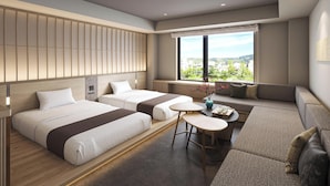 A modern hotel room with two beds, a sofa, a small table, and a view of the city.