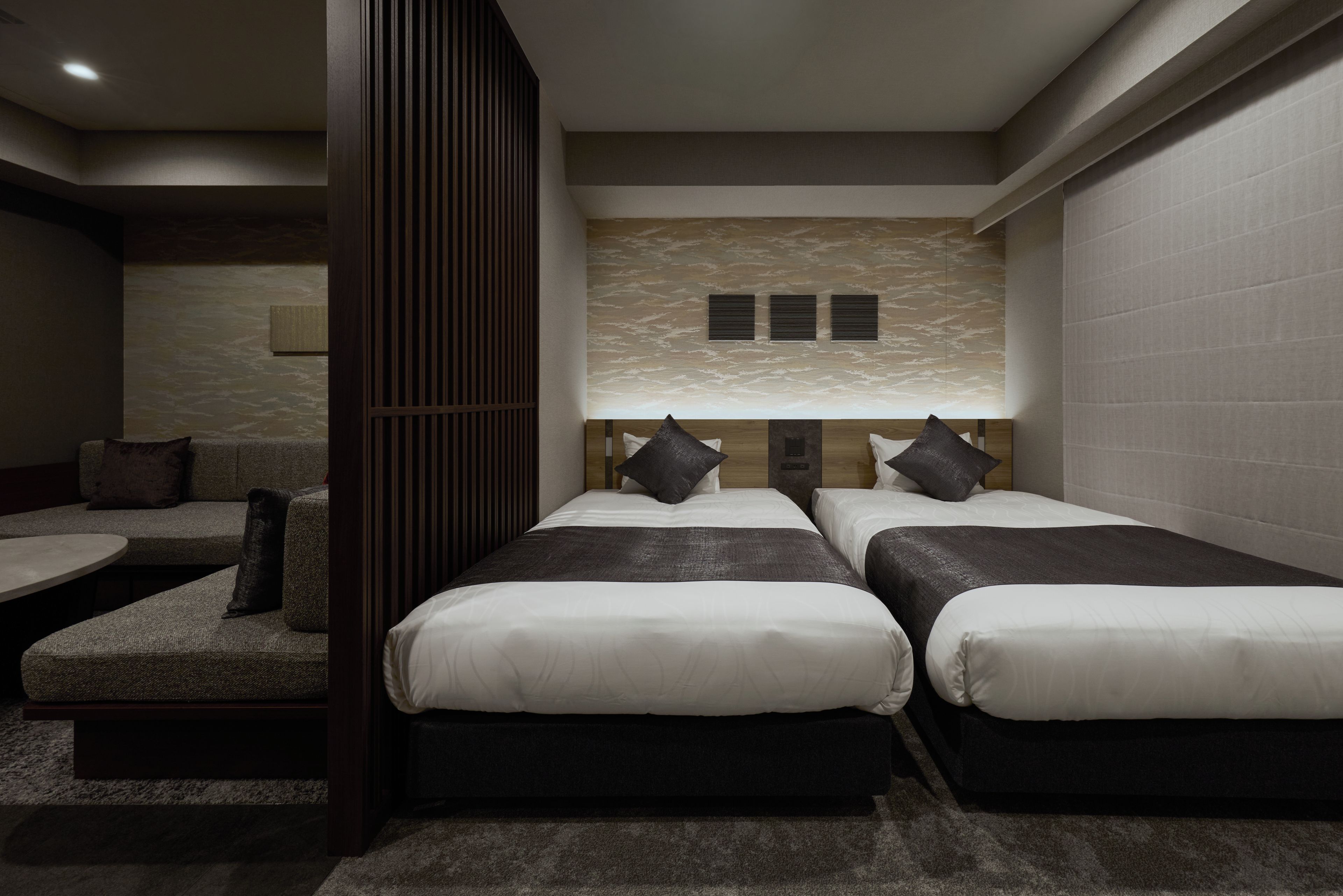 A modern hotel room with two beds, a seating area, and a decorative wall.