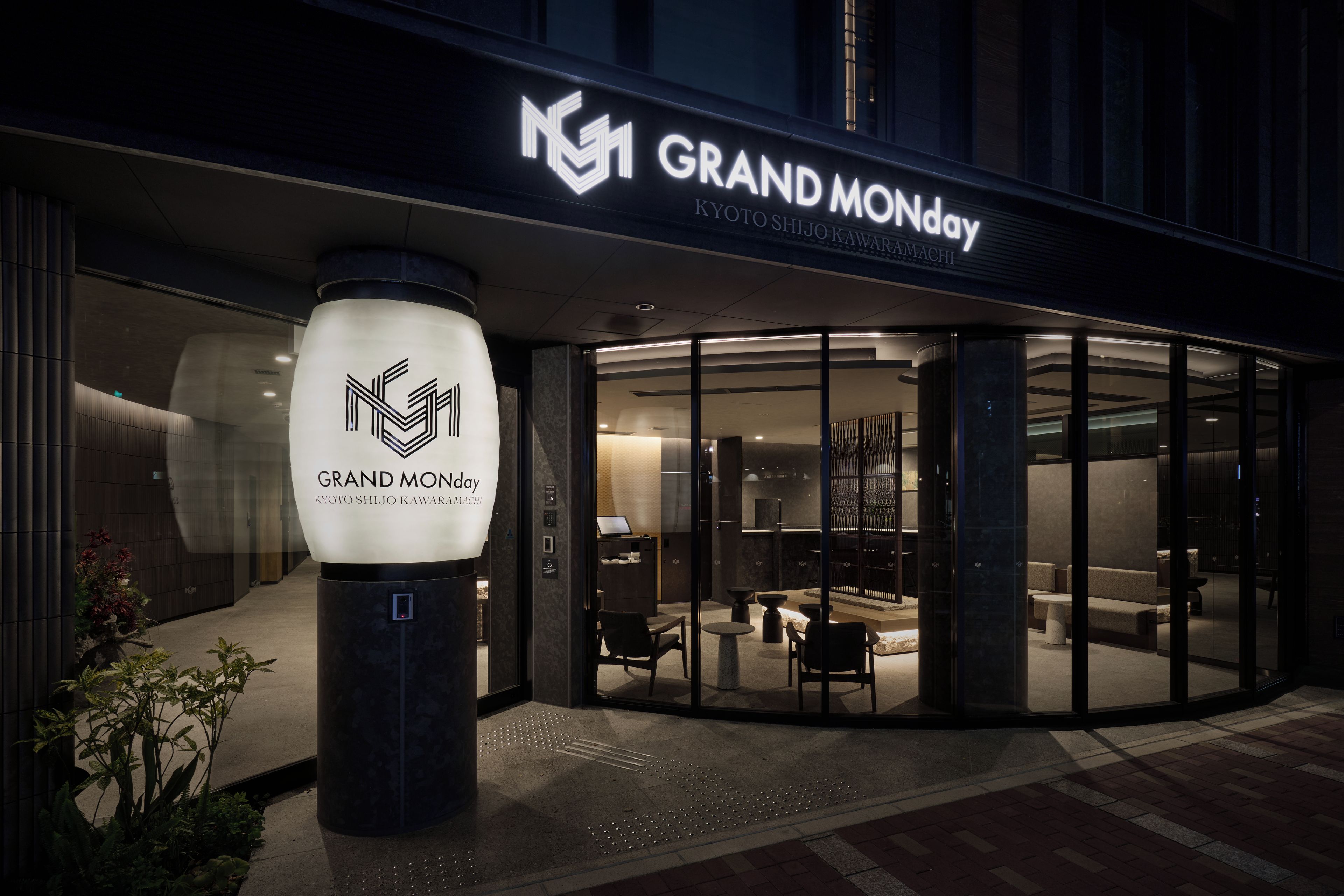 A hotel entrance with a modern design, featuring a glass facade and a prominent illuminated logo.