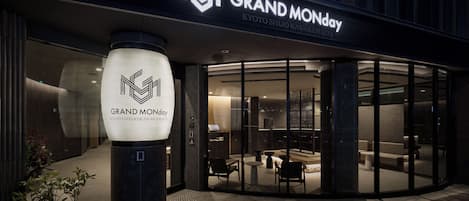 A hotel entrance with a modern design, featuring a glass facade and a prominent illuminated logo.
