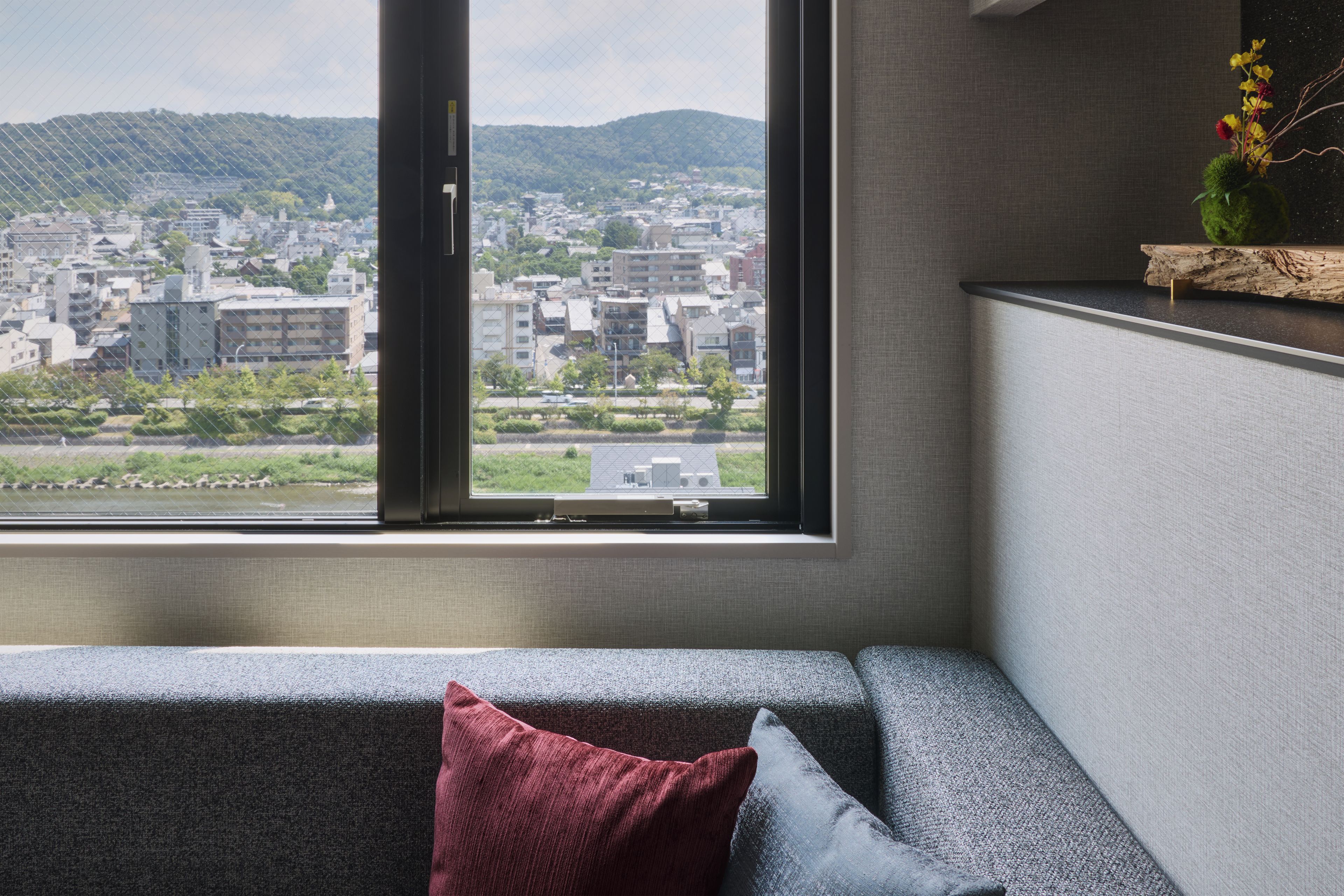 Un intérieur moderne avec un canapé, une fenêtre donnant sur un paysage urbain et une petite plante posée sur une étagère.