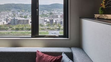 Un interior moderno con un sofá, una ventana que ofrece vistas de la ciudad y una planta pequeña en un estante.