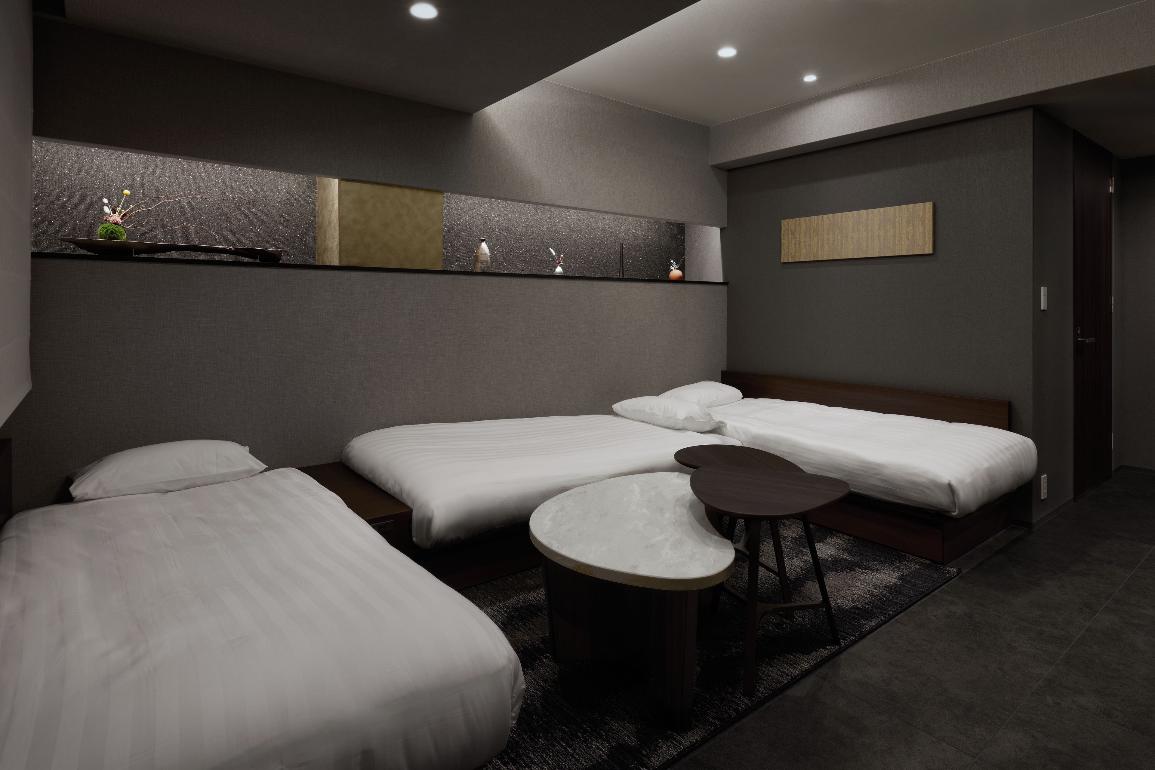 Habitación de hotel con tres camas, una mesita redonda y un estante con adornos.