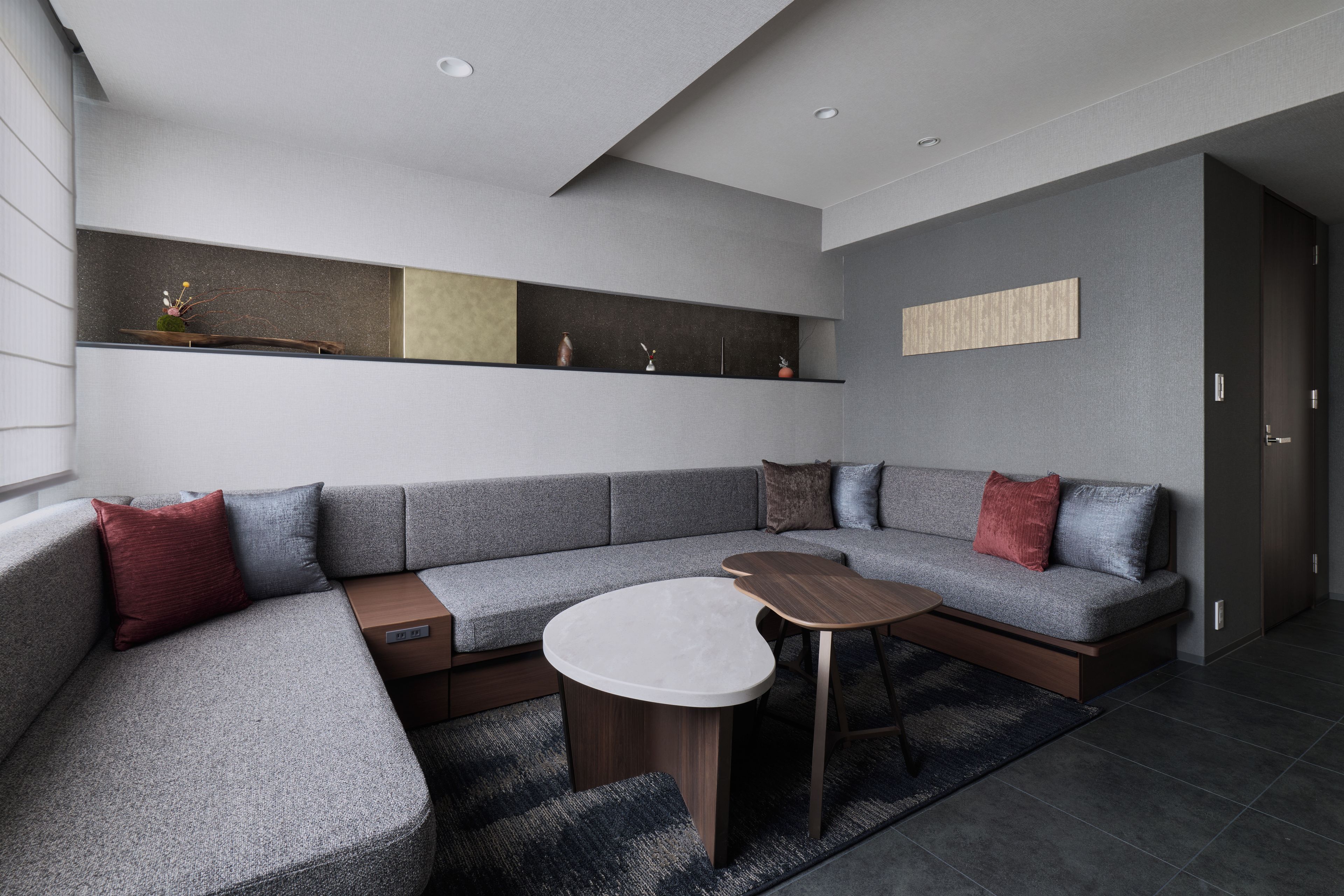 Una sala de estar moderna con un sofá seccional gris, una mesa de centro redonda y estanterías empotradas con objetos decorativos.
