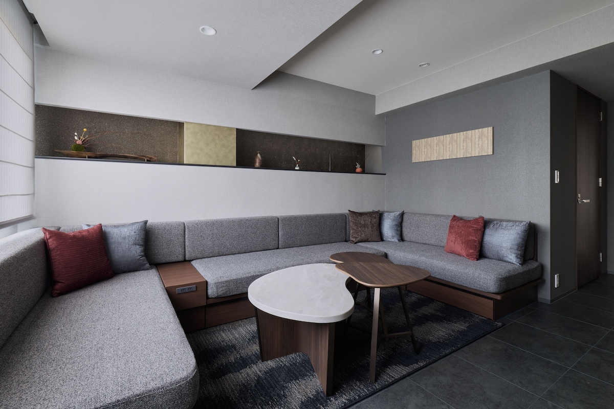 A modern living room with a grey sectional sofa, a round coffee table, and built-in shelving with decorative items.