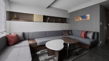 A modern living room with a grey sectional sofa, a small round table, and a decorative shelf with various items.