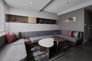 A modern living room with a grey sectional sofa, a small round table, and a decorative shelf with various items. - GRAND MONday KYOTO SHIJO KAWARAMACHI (Kyoto)