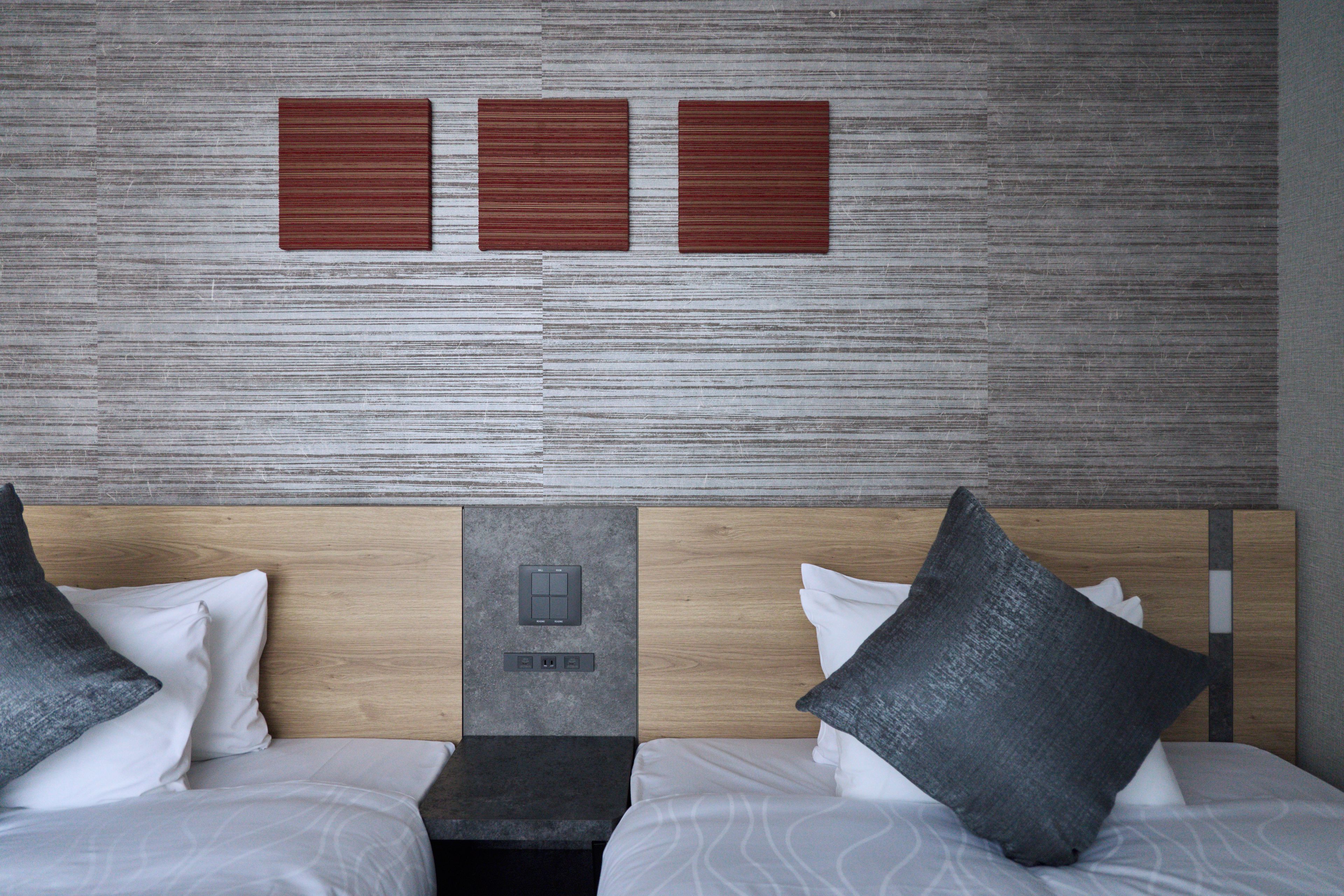 Una habitación de hotel con cabecera de madera, dos camas con ropa de cama blanca y tres paneles en la pared.