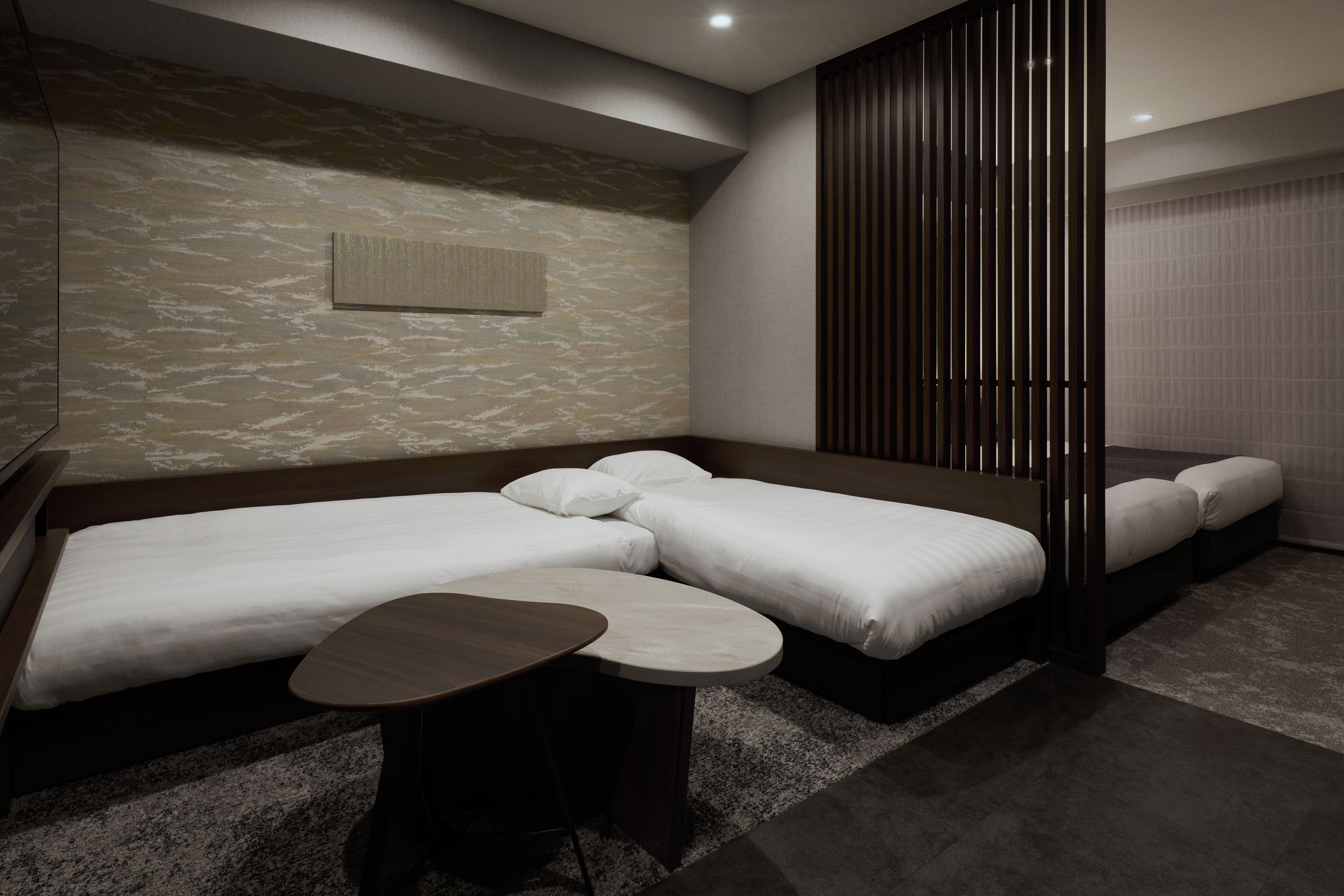 A modern hotel room with a sofa bed, a smaller bed, and a small table.