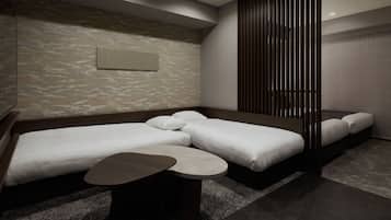 A modern hotel room with a sofa bed, a smaller bed, and a small table.