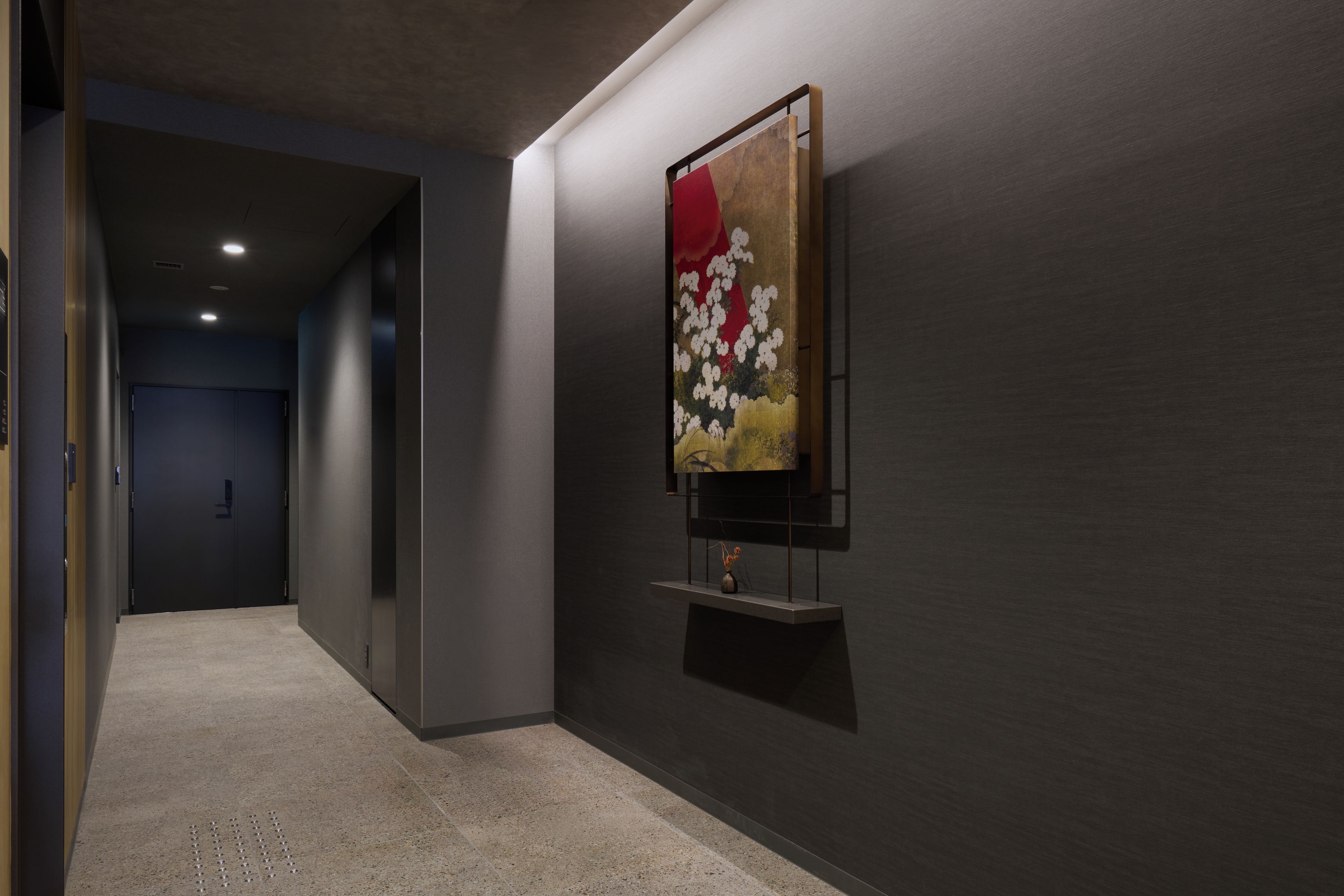 A hallway with a modern art piece on the wall, a door at the end, and a textured floor.