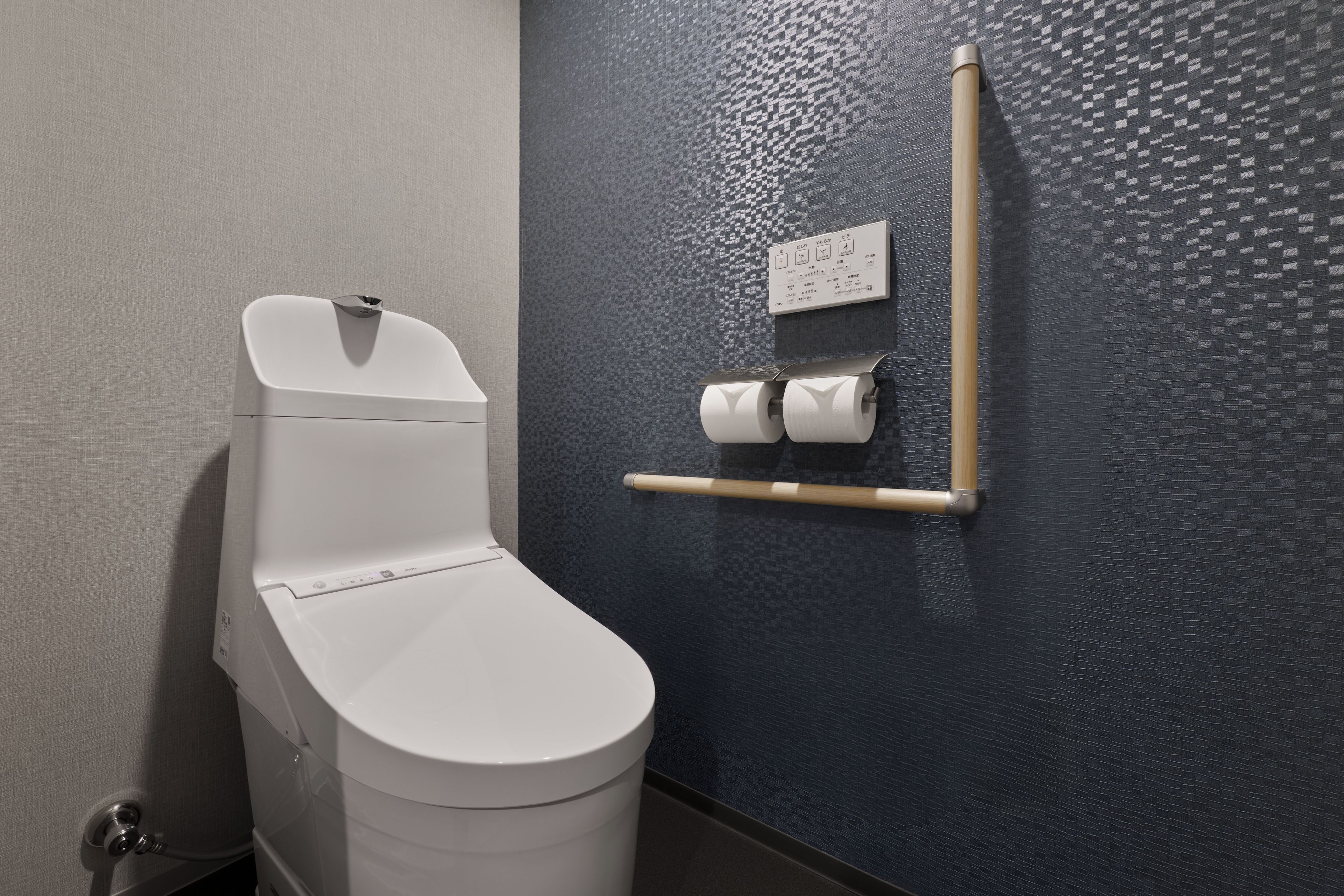 A modern toilet with a control panel, a toilet paper holder, and a bidet control panel on the wall.