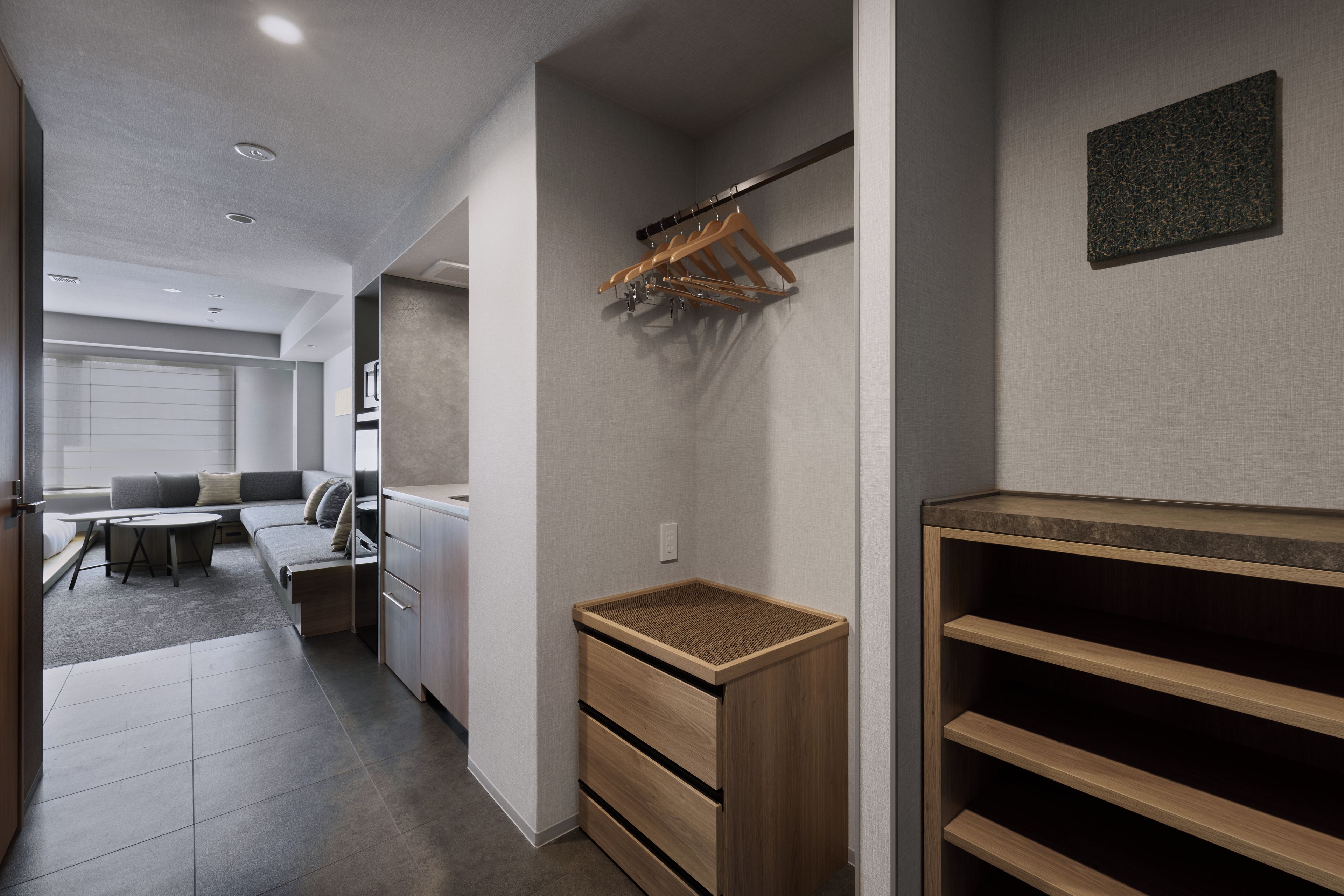 Een modern interieur met een ingebouwde houten plankkast, een zithoek met een bank en een bijzettafeltje, en een gang die naar een andere kamer leidt.