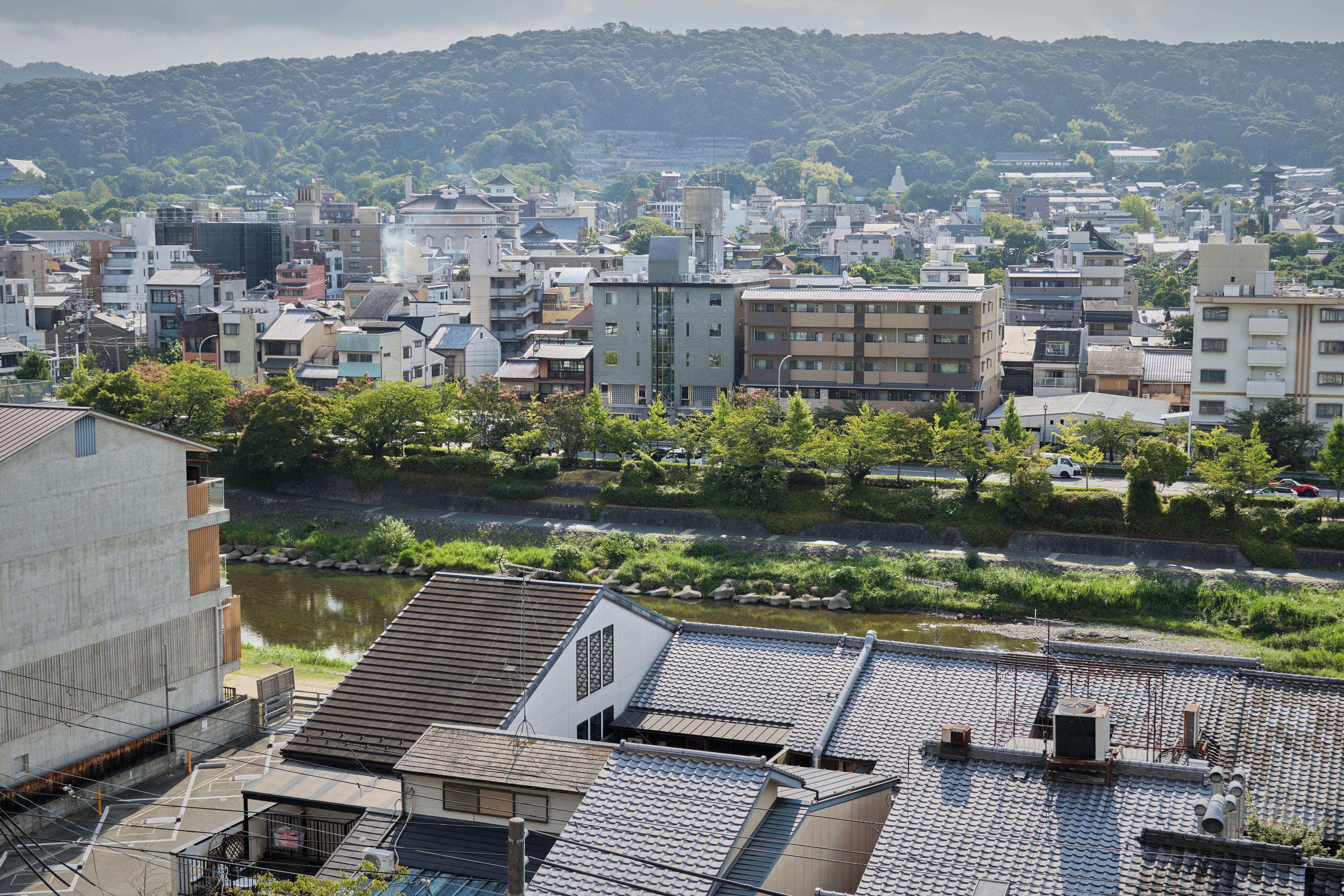 A cityscape with traditional and modern buildings, a river, and a hilly backdrop.