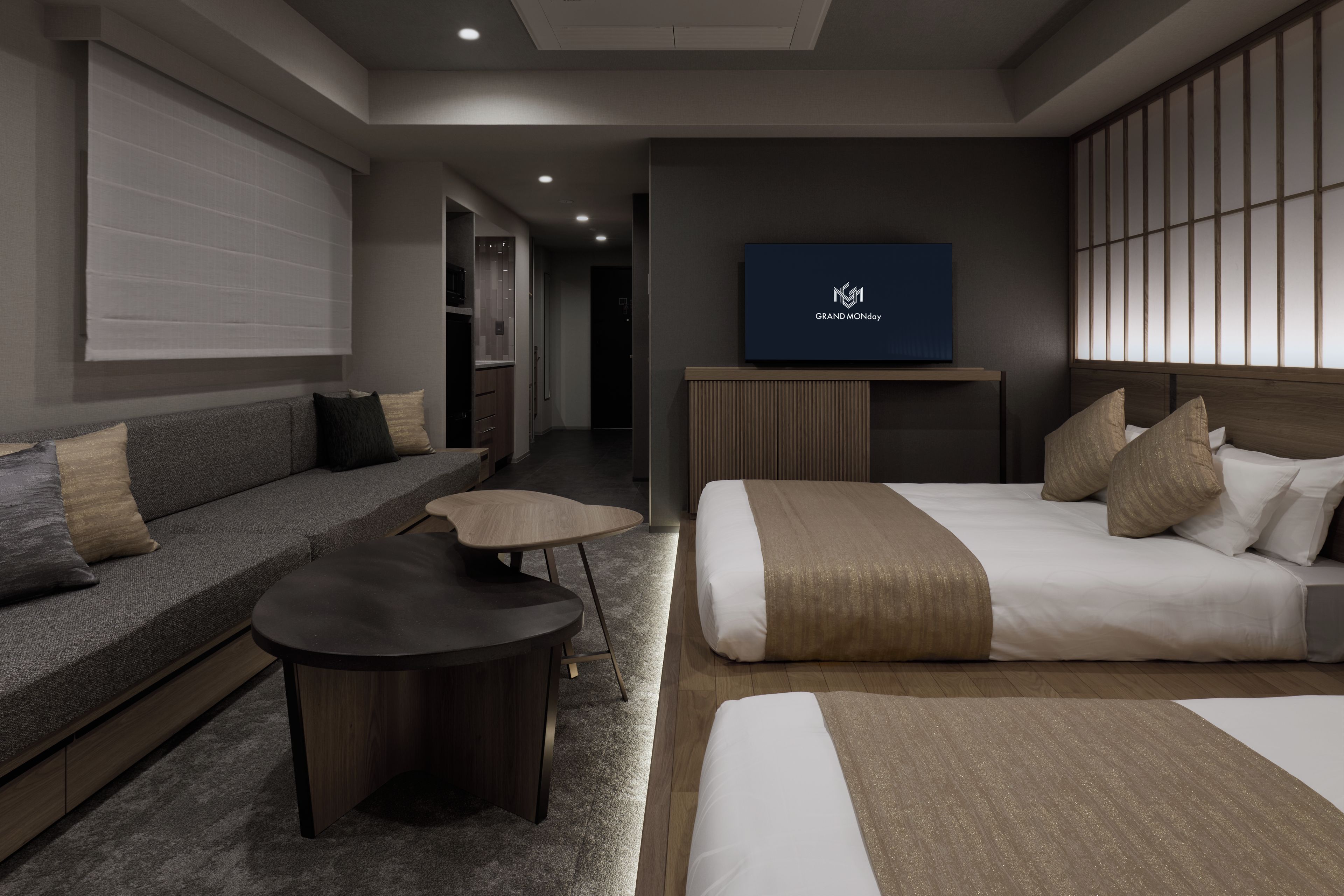 A modern hotel room with a sofa, a bed, a small table, and a TV on the wall.