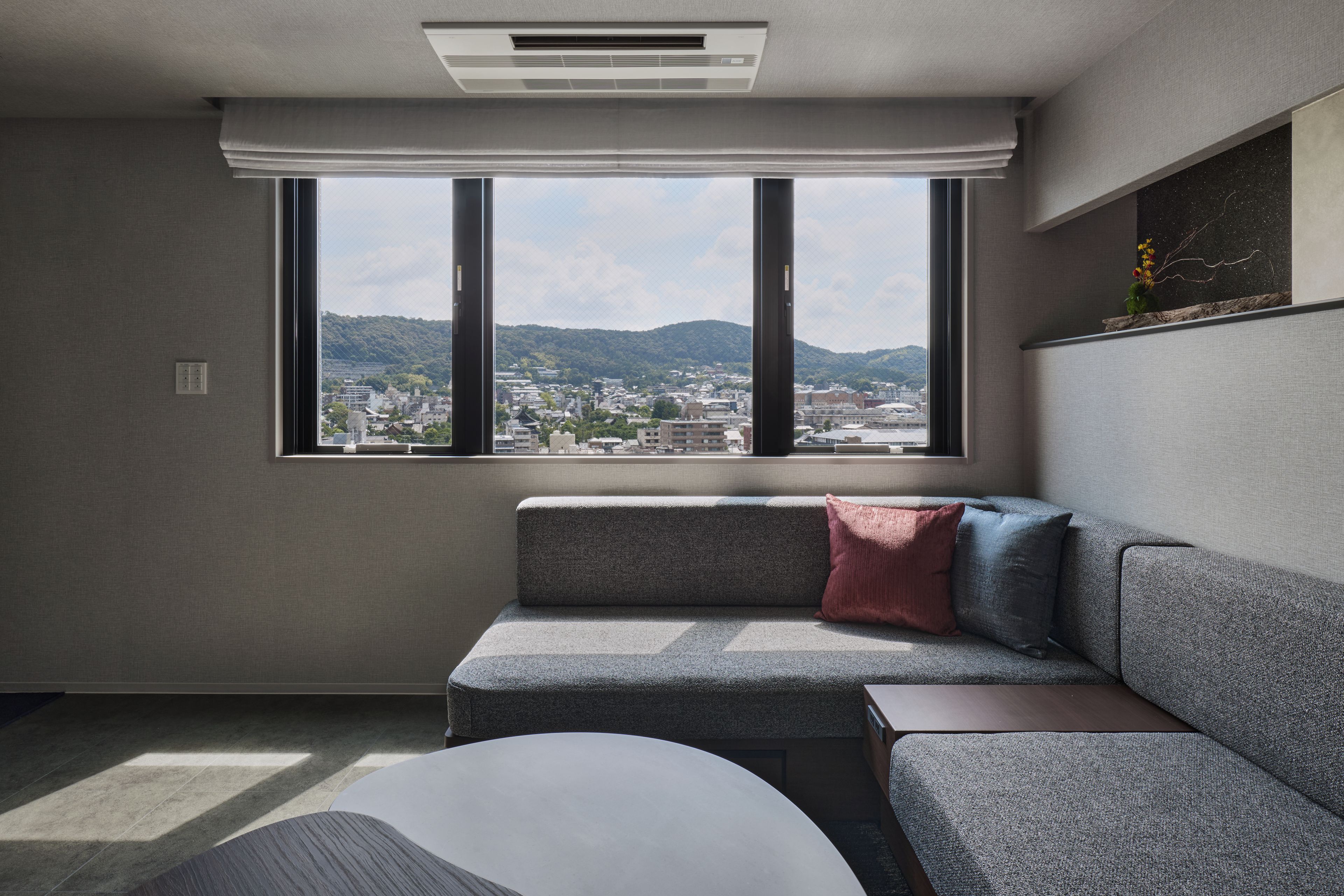 A modern living room with a sofa, a small table, and a large window offering a city view.