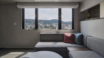 A modern living room with a sofa, a small table, and a large window offering a city view.