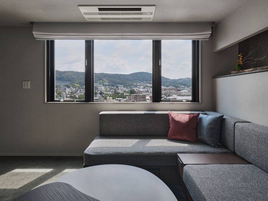 A modern living room with a sofa, a small table, and a large window offering a city view.
