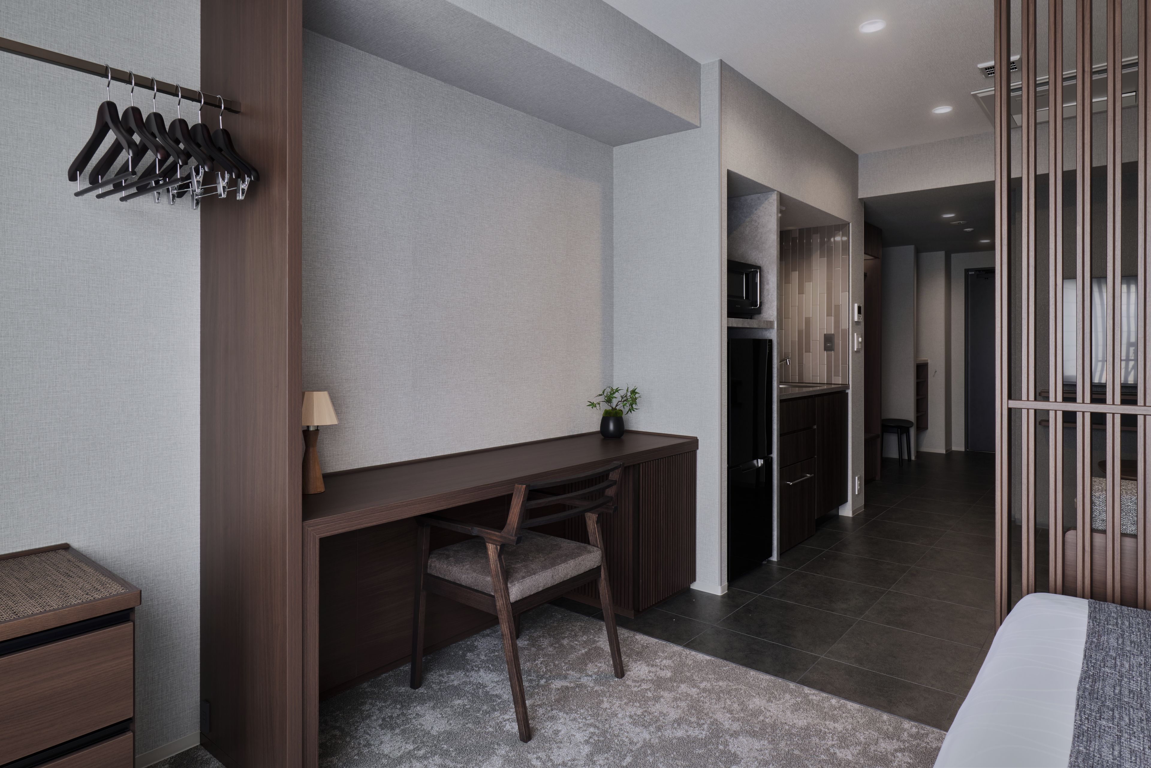 Una moderna camera d'hotel con una scrivania in legno, una sedia, una piccola pianta e un letto con copripiumino grigio e bianco.