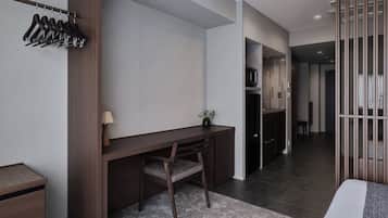 Habitación de hotel moderna con un escritorio de madera, una silla, una planta pequeña y una cama con colcha gris y blanca.