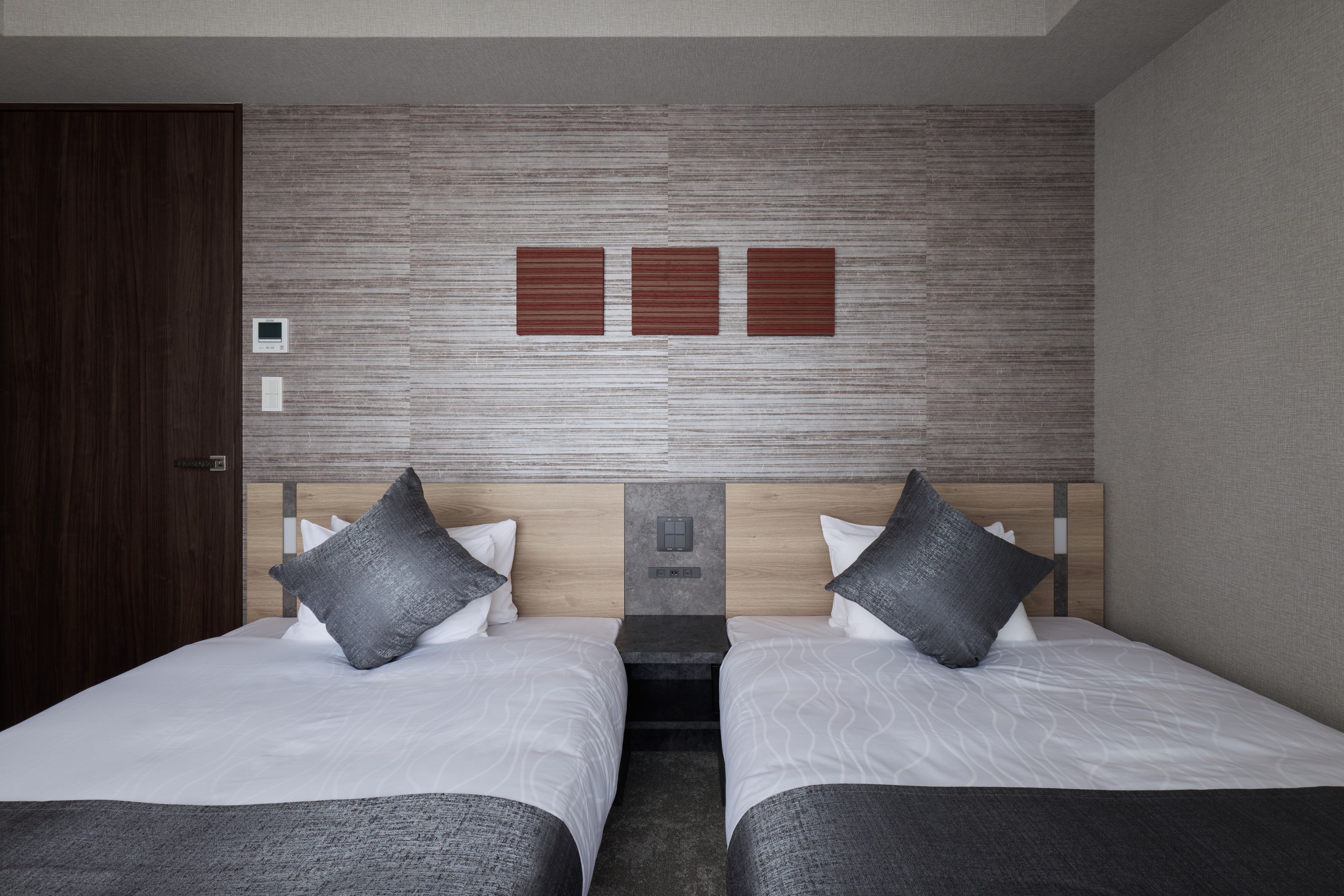 A hotel room with two beds, a wooden headboard, and a control panel on the wall.