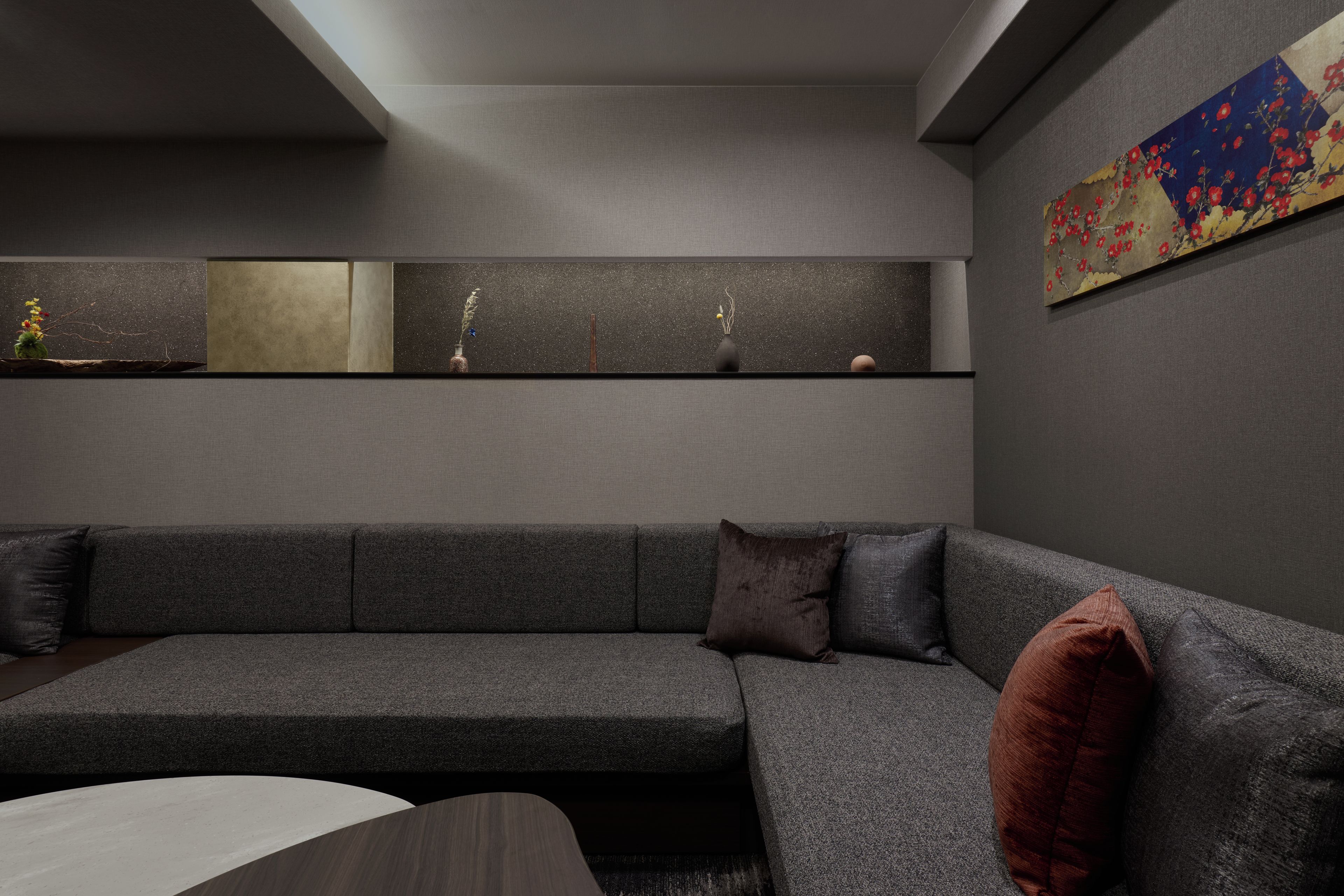A modern living room with a grey sofa, a coffee table, and a wall-mounted shelf with decorative items.