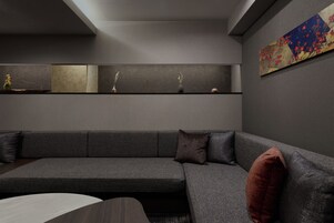 A modern living room with a grey sofa, a coffee table, and a wall-mounted shelf with decorative items.