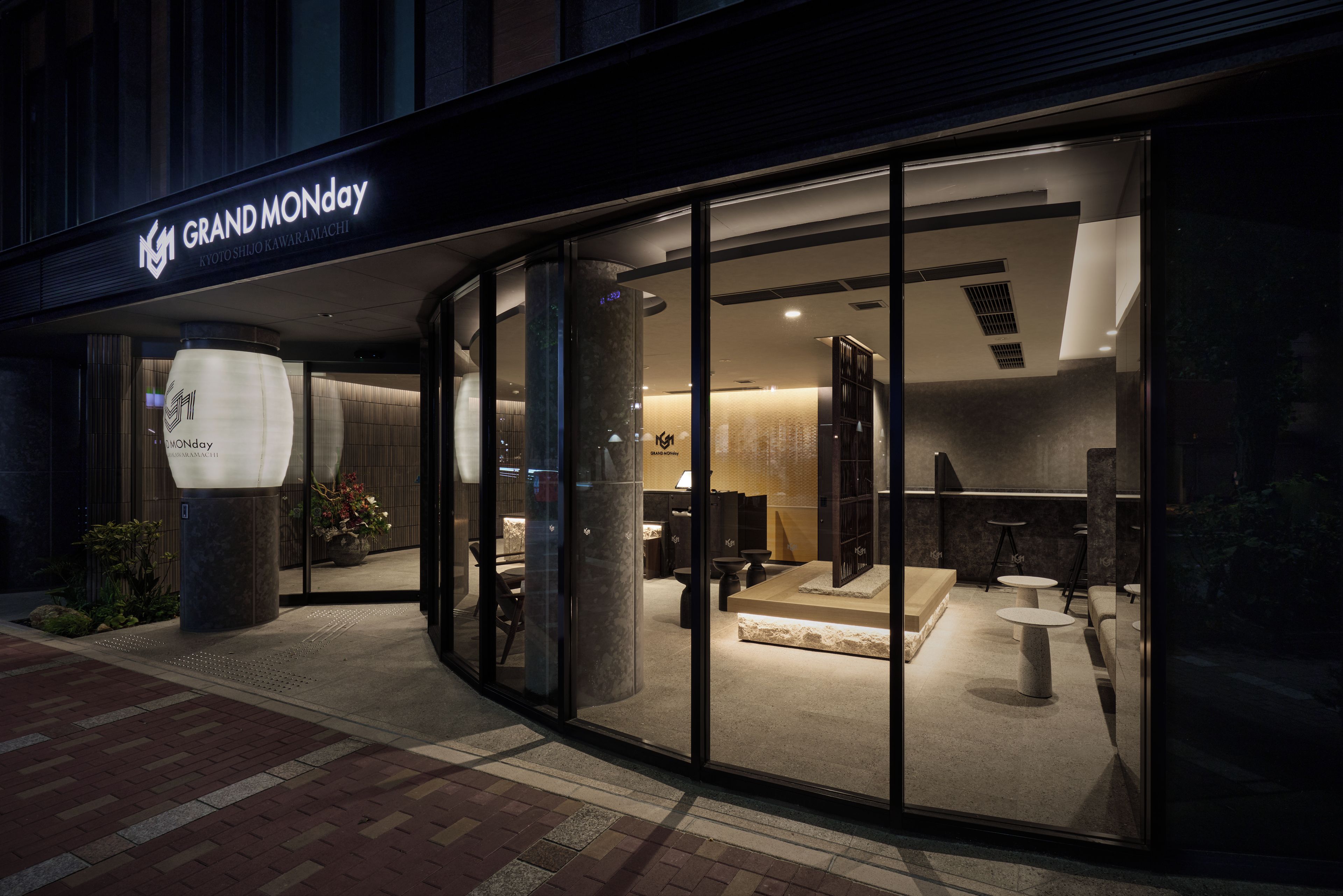 A modern hotel entrance with glass doors, a reception desk, and a seating area visible inside.