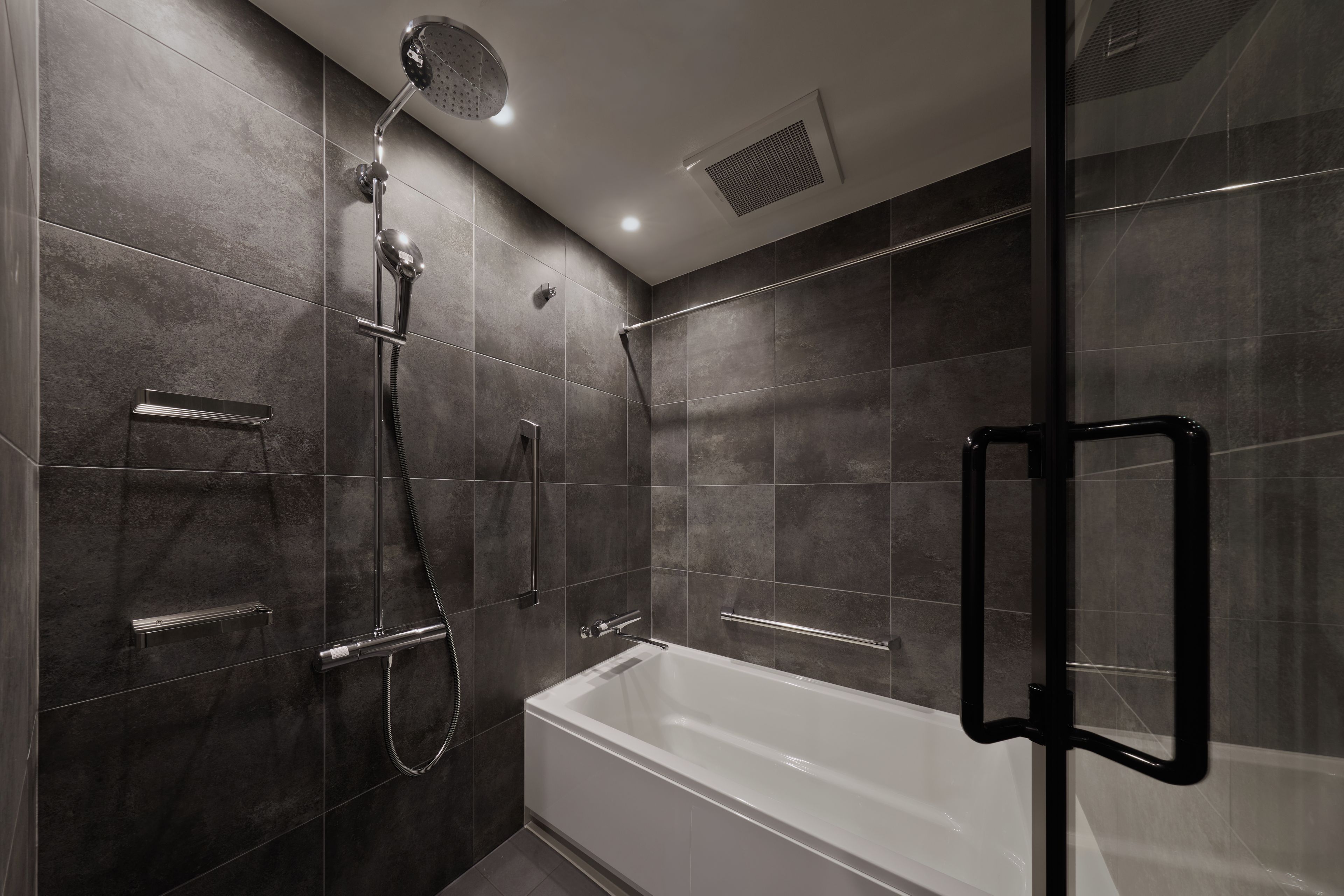 A modern bathroom with a glass-enclosed shower, a white bathtub, and a handheld showerhead.