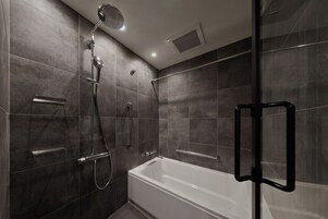 A modern bathroom with a glass-enclosed shower, a white bathtub, and a handheld showerhead.