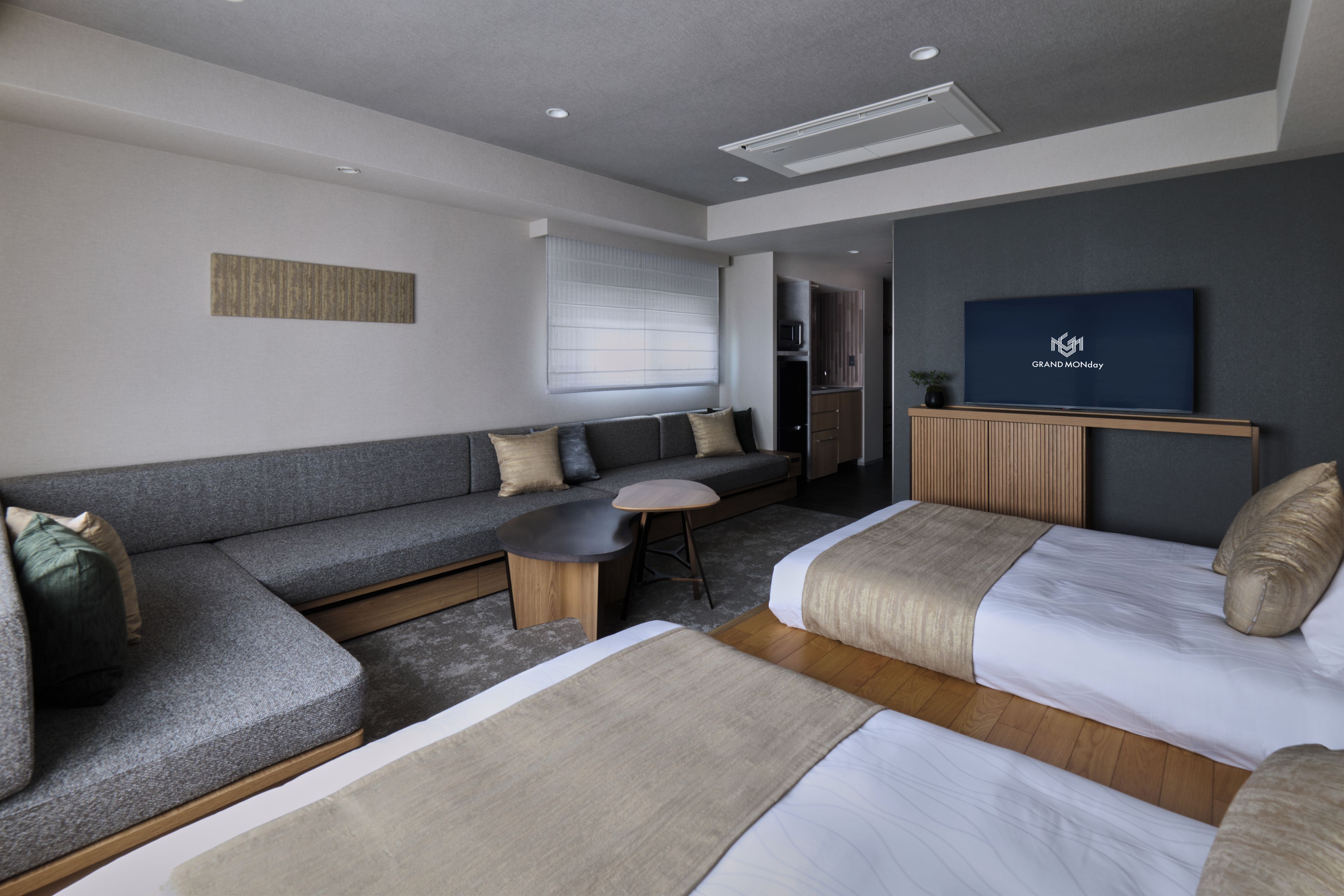 A modern hotel room with a sofa, a bed, a small table, and a television.