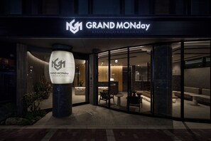 The exterior of a hotel with a modern facade, a prominent illuminated logo, and a reception area visible through the glass doors. - GRAND MONday KYOTO SHIJO KAWARAMACHI (Kyoto)