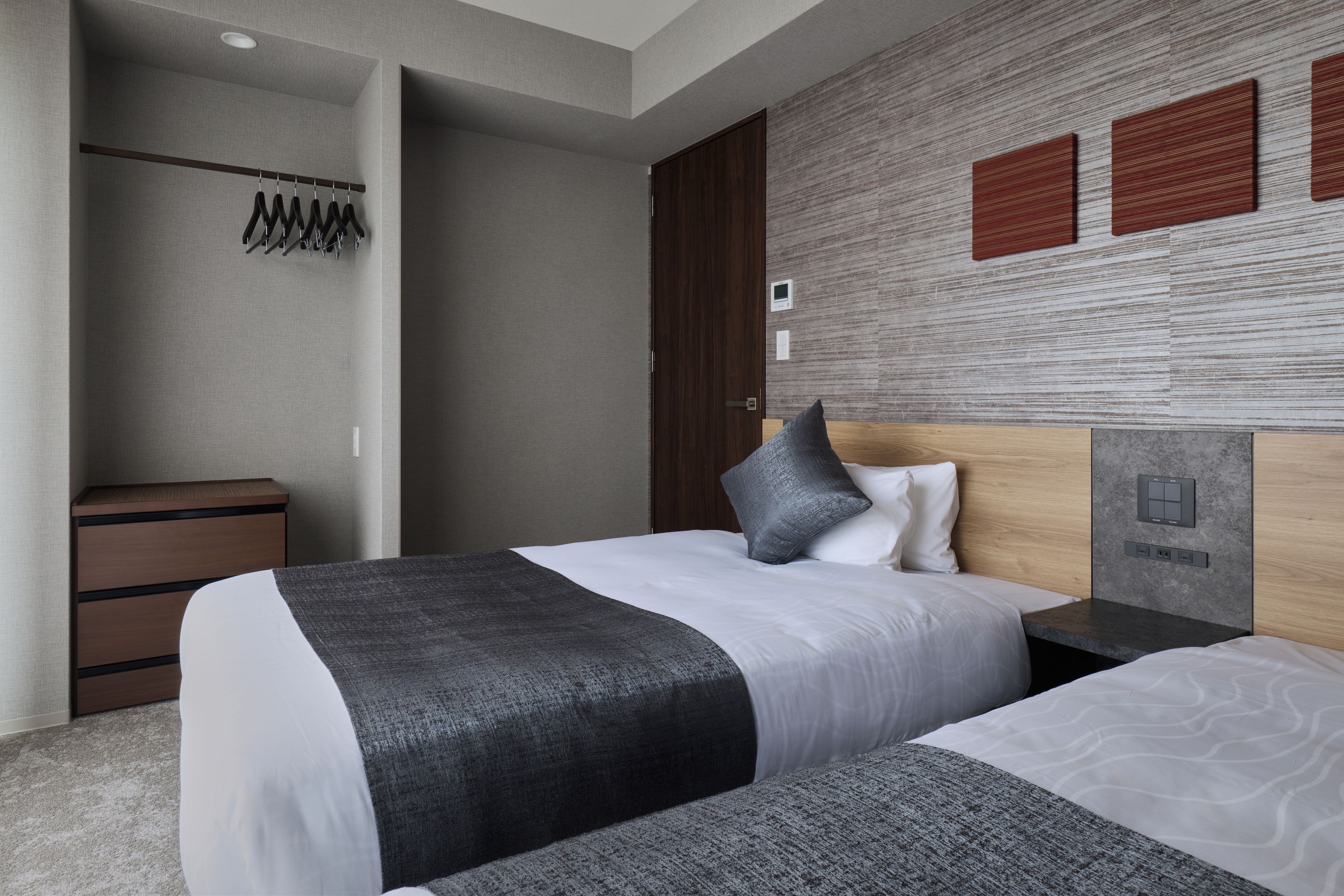 Une chambre d’hôtel comprenant un lit, des tables de chevet, une armoire et un panneau de commande fixé au mur.