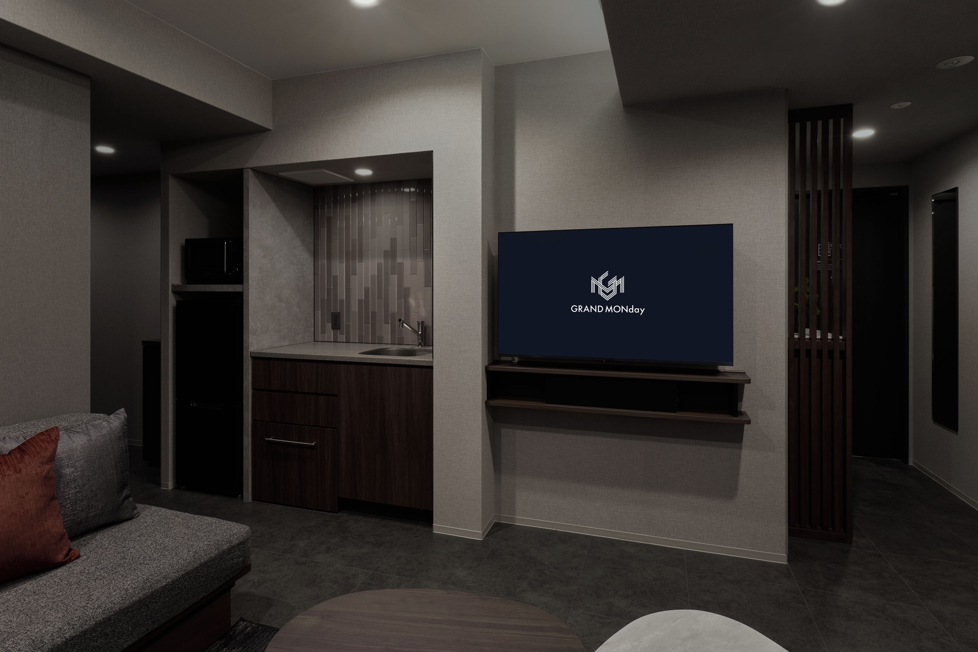 Una sala de estar moderna con un televisor de pantalla plana montado en la pared, un mueble de madera oscura, un sofá gris con un coj ín rojo y una pequeña mesa redonda.