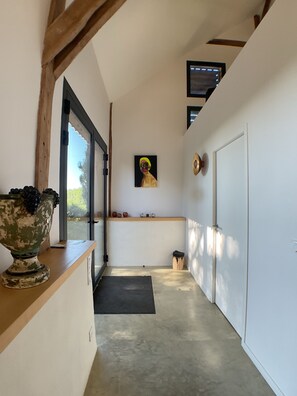 Un couloir étroit avec un banc en bois, un grand vase et une œuvre d’art encadrée accrochée au mur.