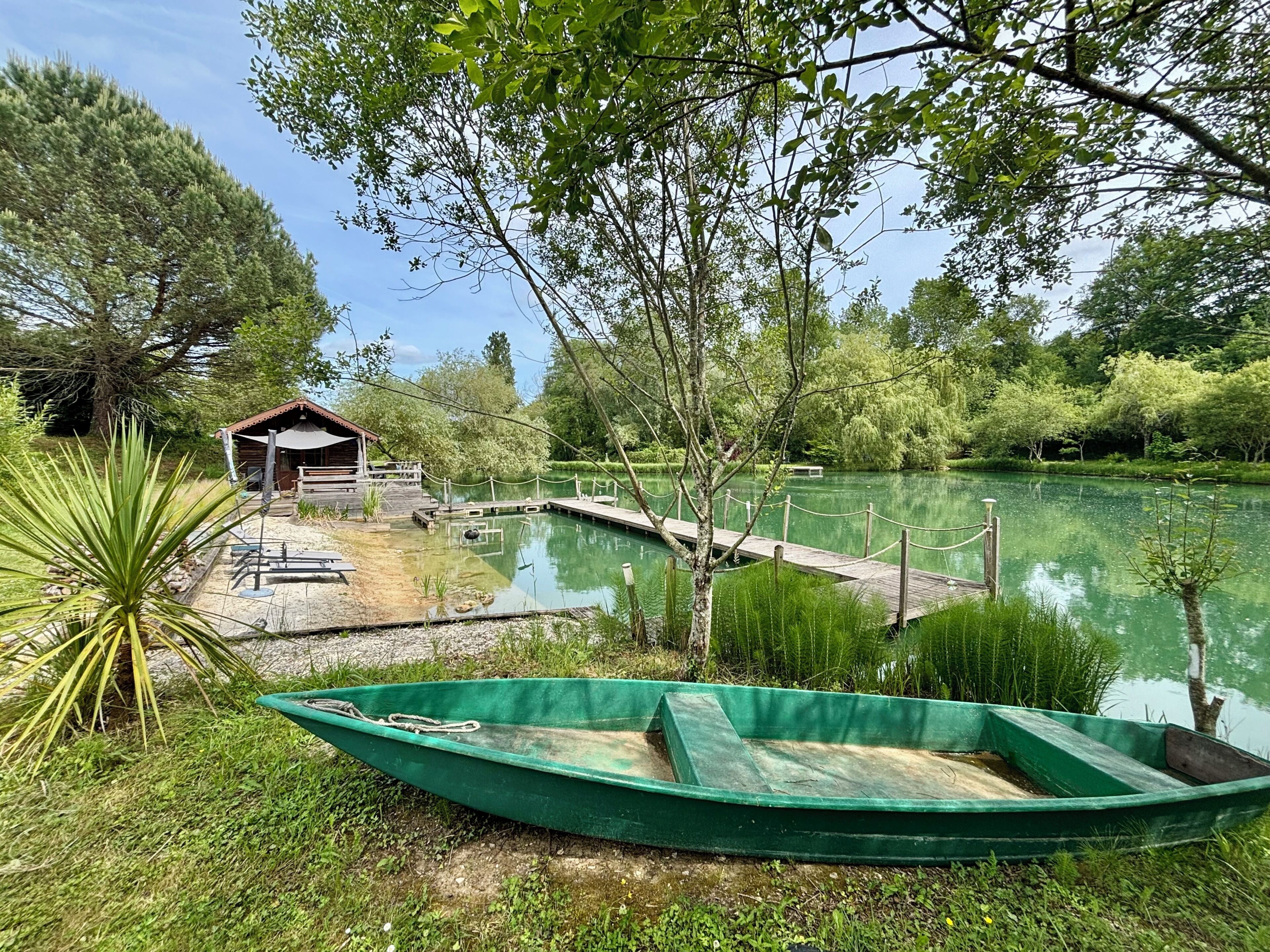 Eine idyllische Seelage mit einem Holzsteg, einem kleinen Pavillon und einem grünen Boot.