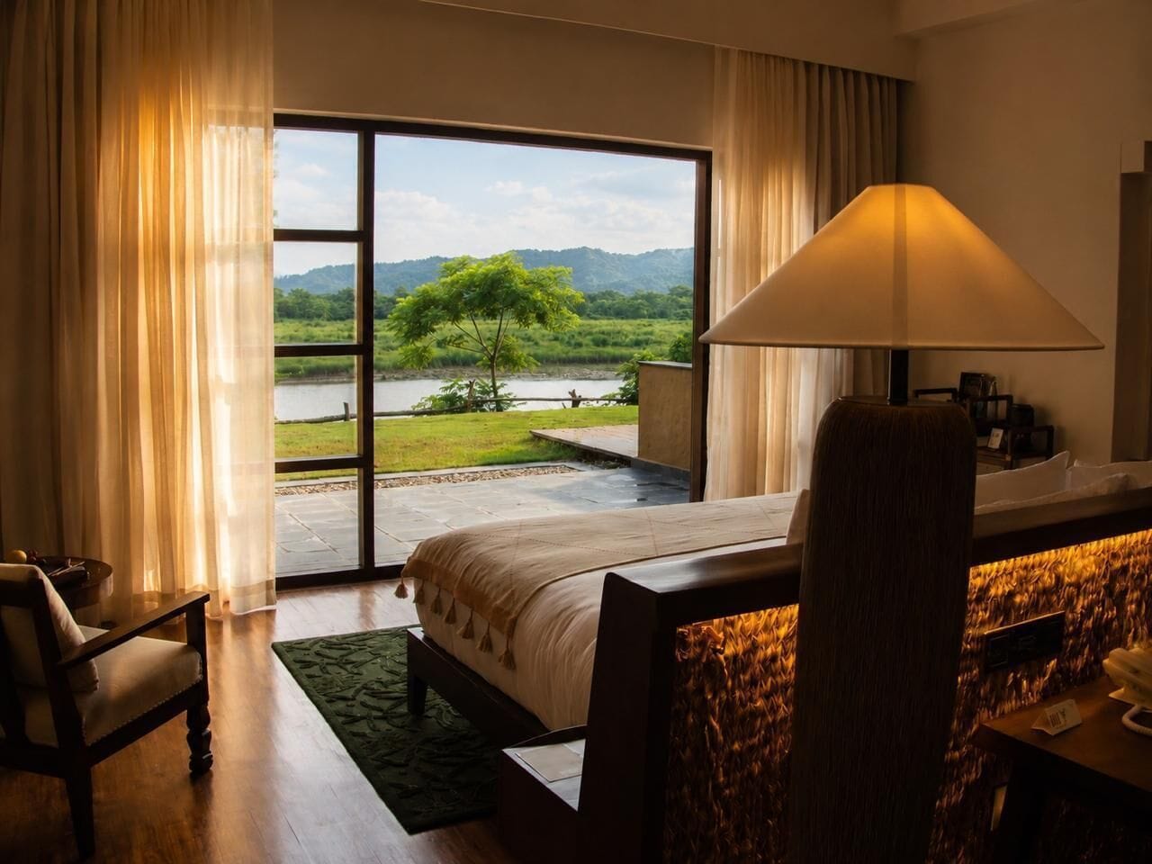 Habitación de hotel con cama, escritorio, silla, lámpara y vistas a un lago y montañas.