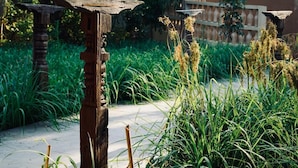 A rustic outdoor area with a wooden structure, possibly a bench or a decorative piece, surrounded by lush greenery and a pathway.